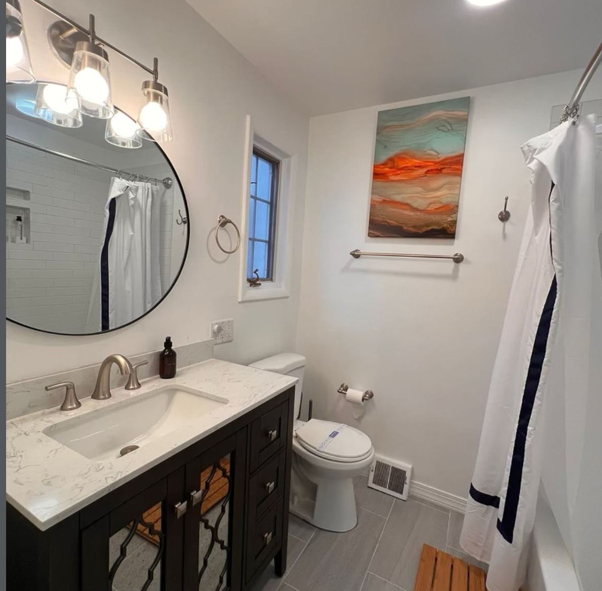 Bathroom with dark vanity, round mirror, and grey tile