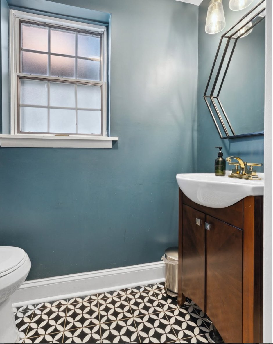 Powder room with teal walls, patterned floor tile, and a gold faucet