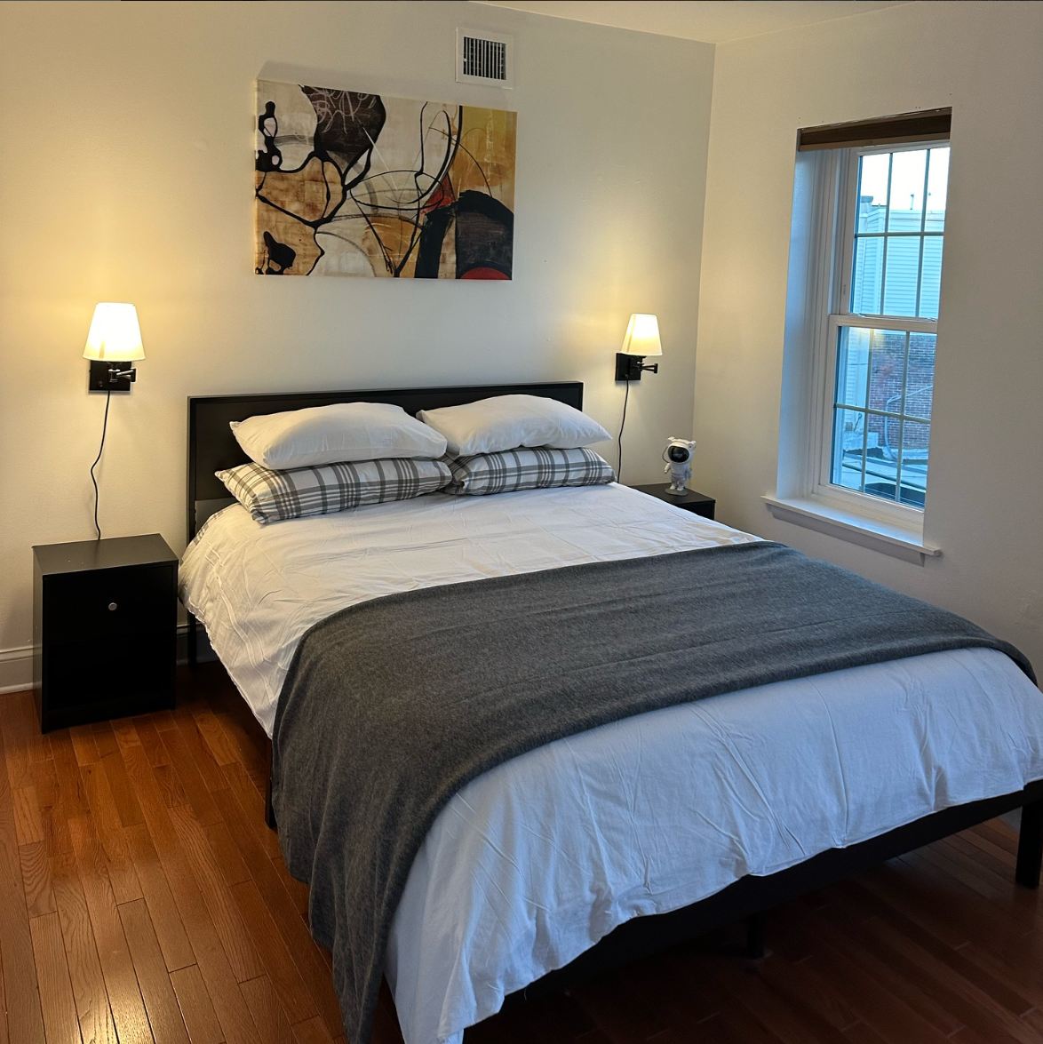 Bright bedroom with white linens, wall sconces, and artwork above the bed