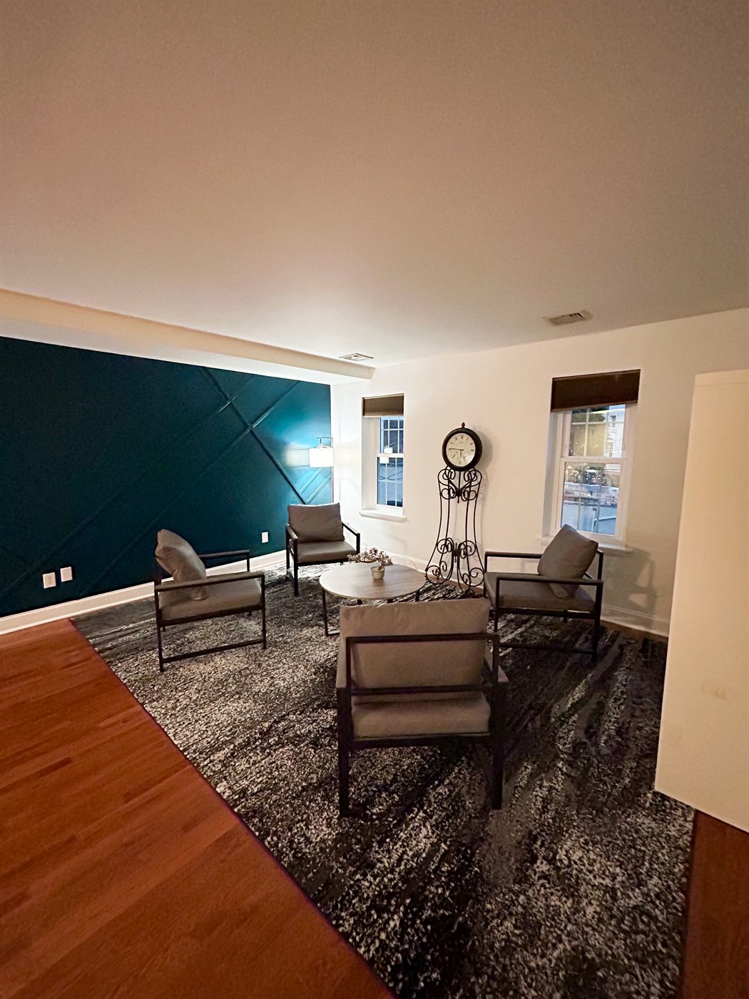 Living area with four grey chairs, round wood table, and teal accent wall