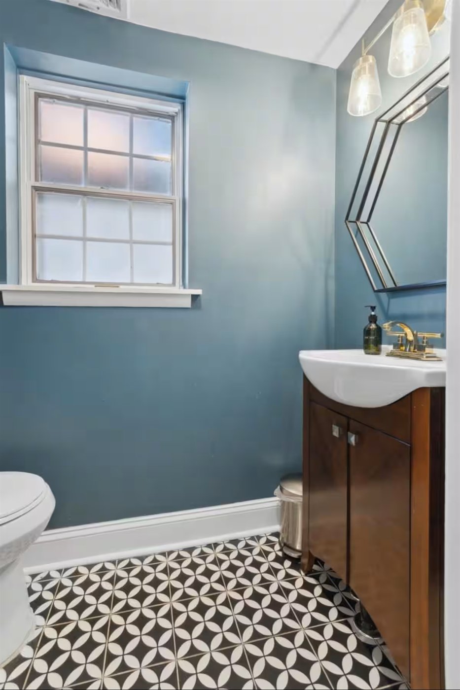 Powder room with teal walls, patterned floor tile, and a gold faucet