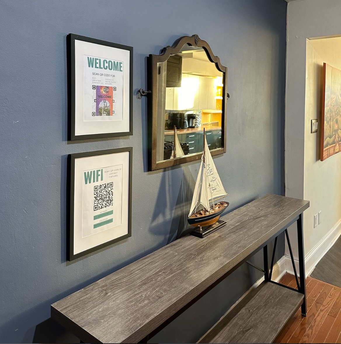 Entry console with sailboat, mirror, and guest information on a teal wall