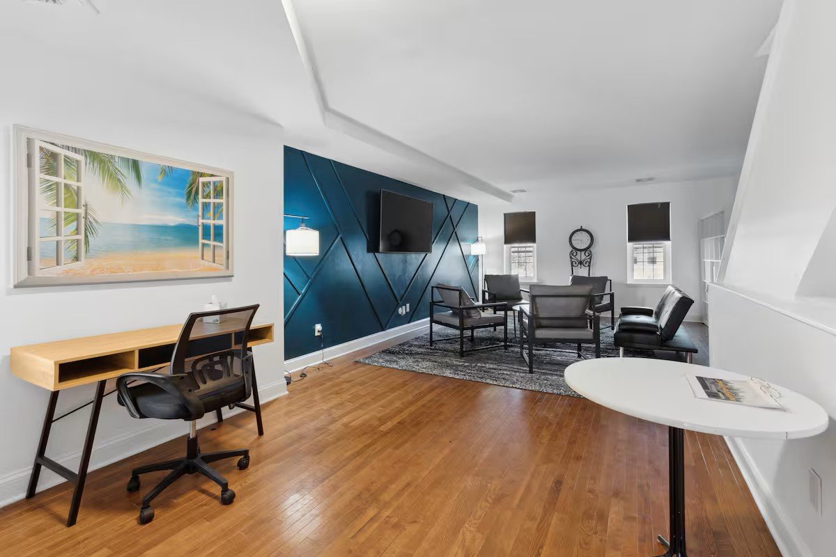 Living room with teal geometric accent wall, seating, and a desk