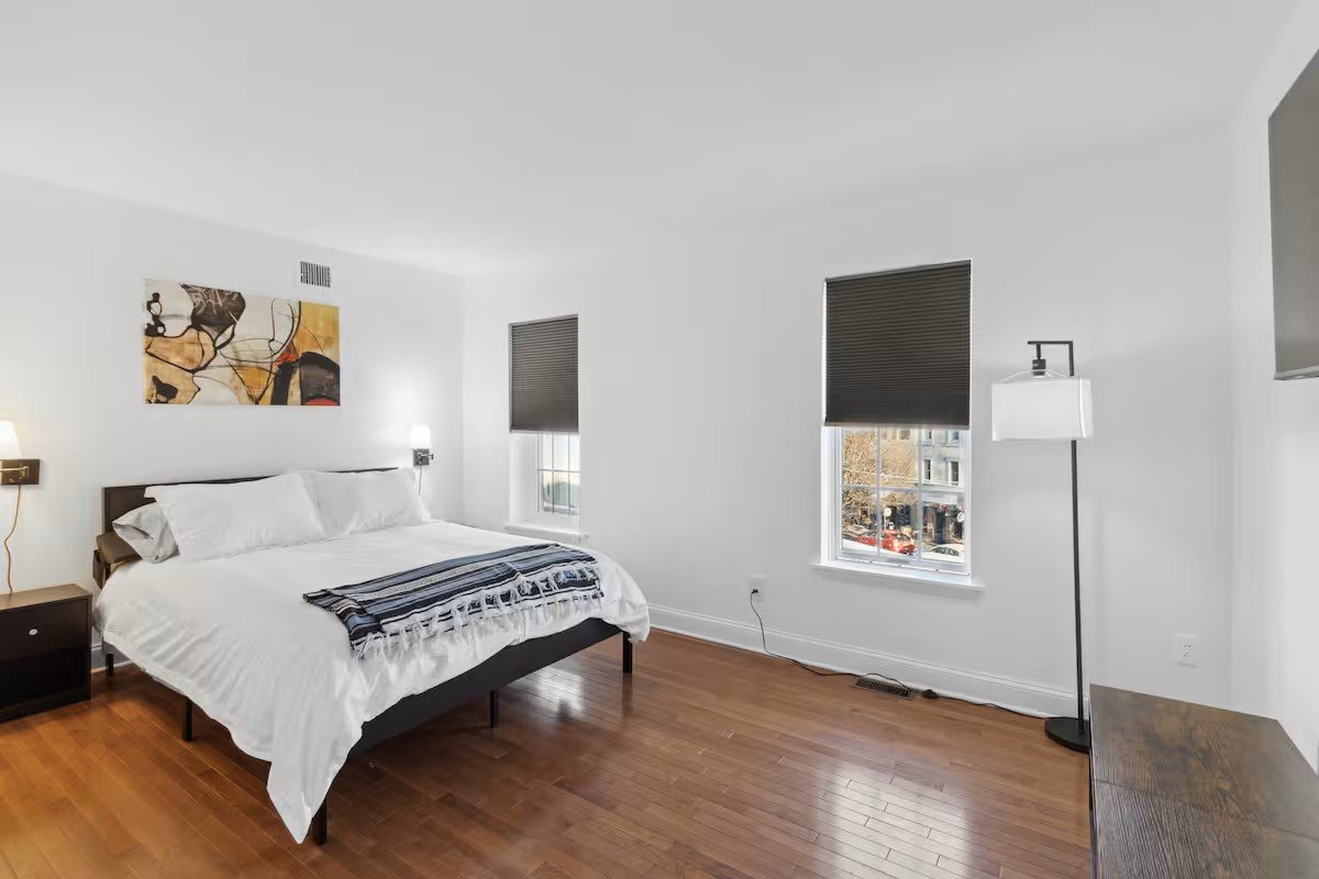 Second bedroom with white linens, abstract artwork, and windows