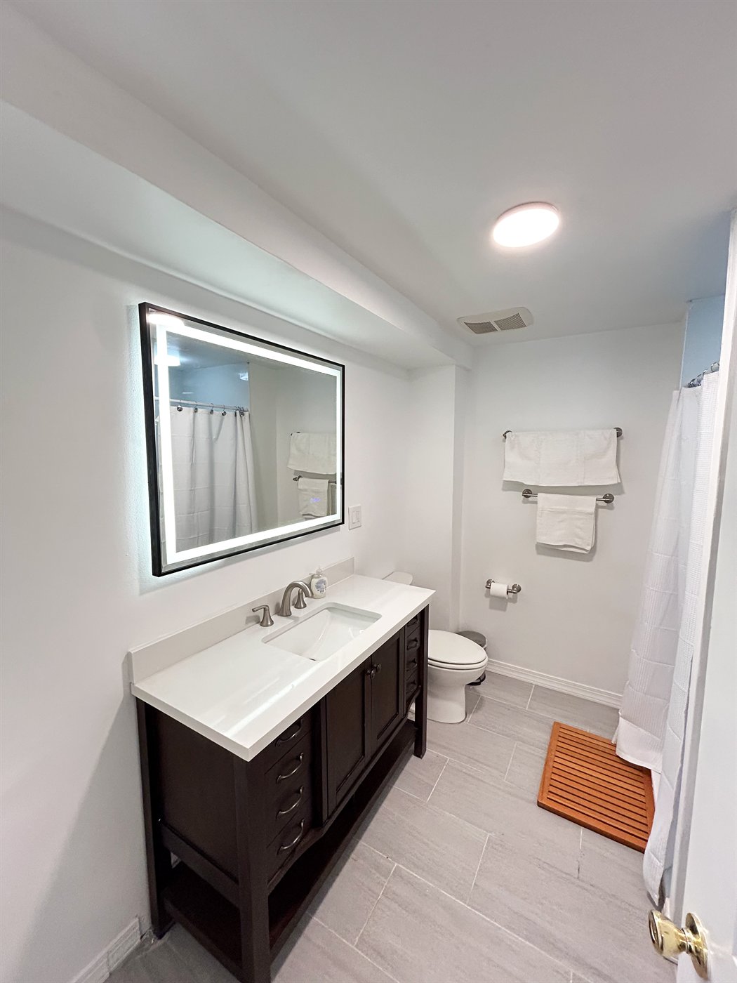Bathroom vanity with dark wood cabinets and an illuminated mirror